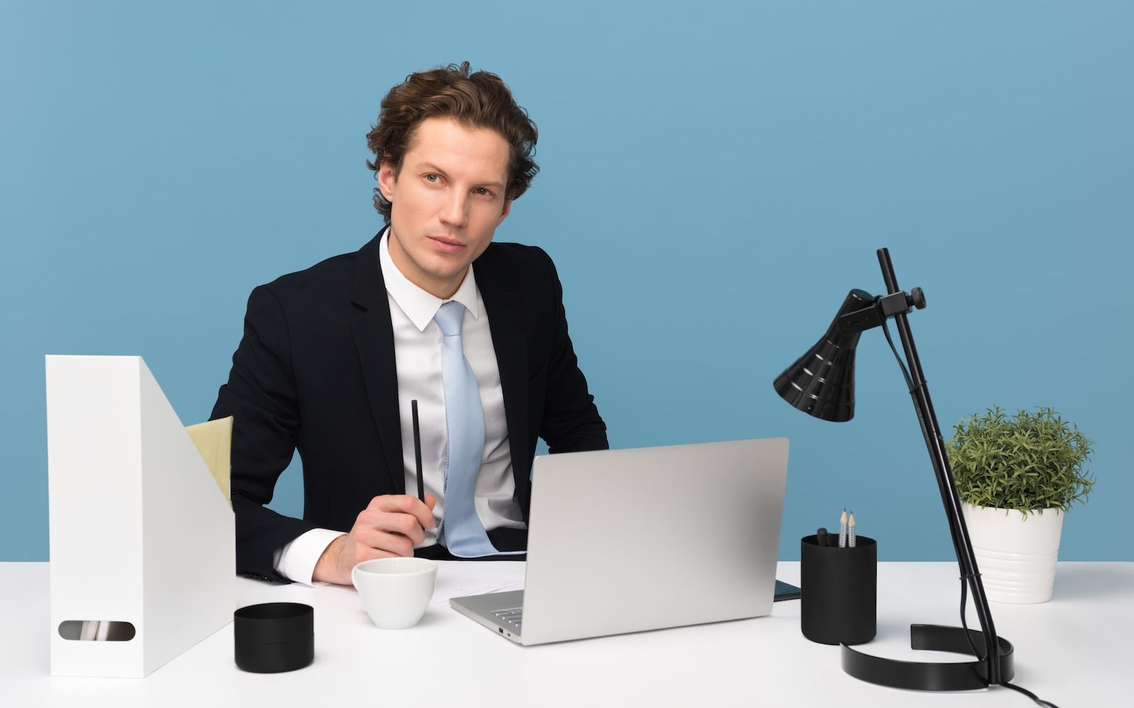 man sitting on chair beside laptop computer and teacup